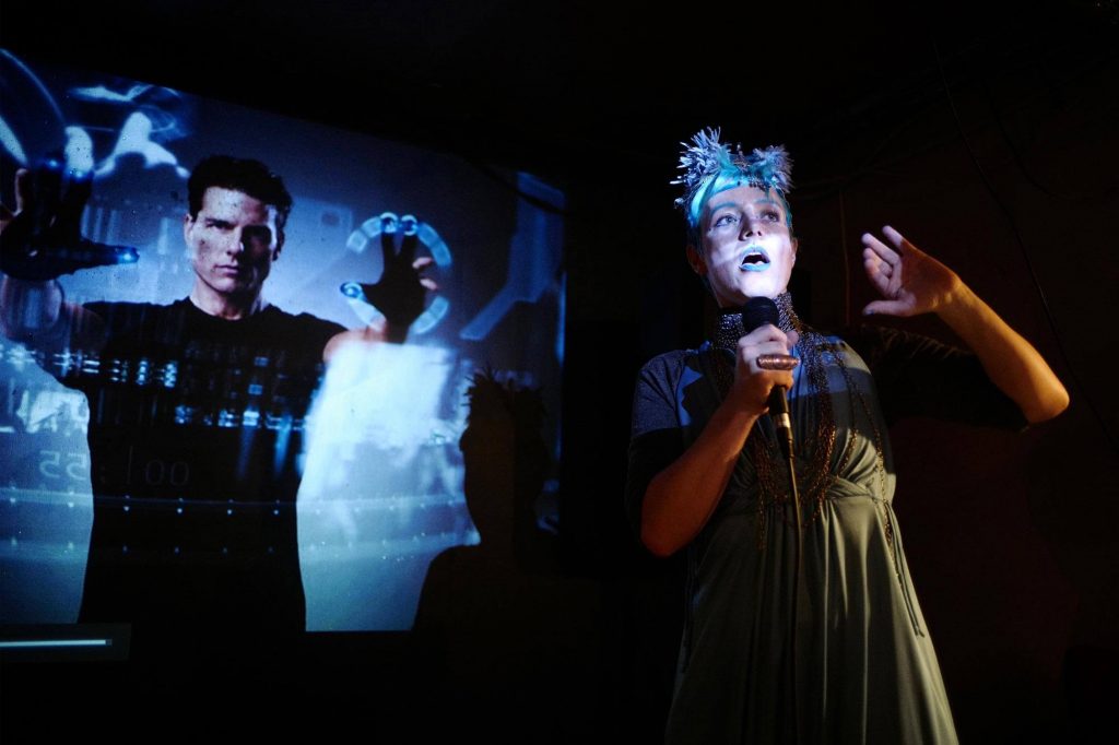 Woman with microphone on stage, a movie scene in the backdrop.